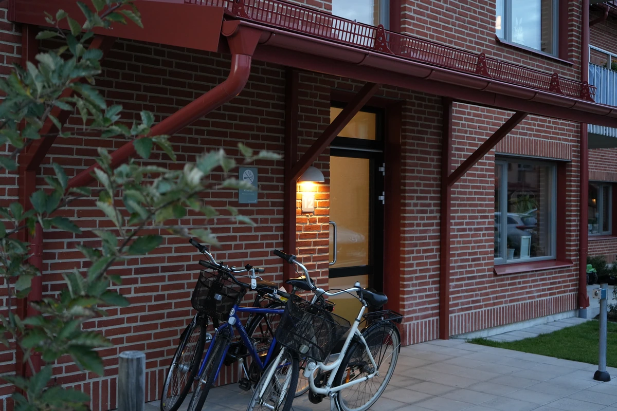 Väduren · entrédetalj med tegel, belysning och cyklar.